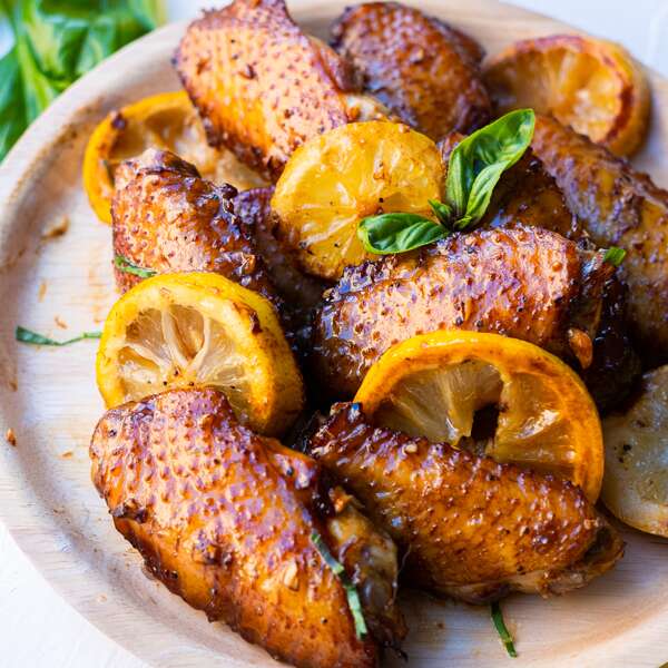 Baked honey lemon chicken wings served in a wooden plate with lemon slices and basil leaves.