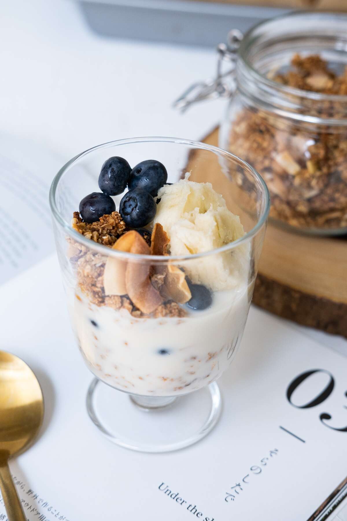 Serve granola with fresh blueberries, banana and milk in a glass.